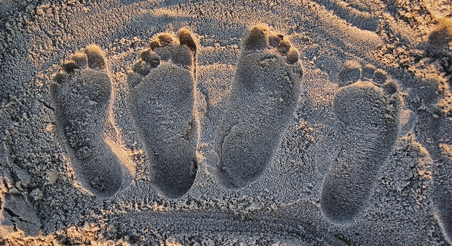 Fire fodspor i sandet ved stranden – et symbol på indre ro, stressreduktion, angsthåndtering, grounding og heling af traumer gennem naturbaseret walk-and-talk psykoterapi.